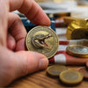 A hand holds a gold-colored collectible coin featuring an alligator design on a wooden surface.
