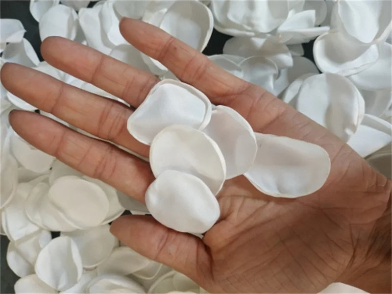 A hand holds a cluster of white silk rose petals for weddings and events.