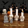 A set of resin skull candle holders with lit candles in front of a spooky castle silhouette.