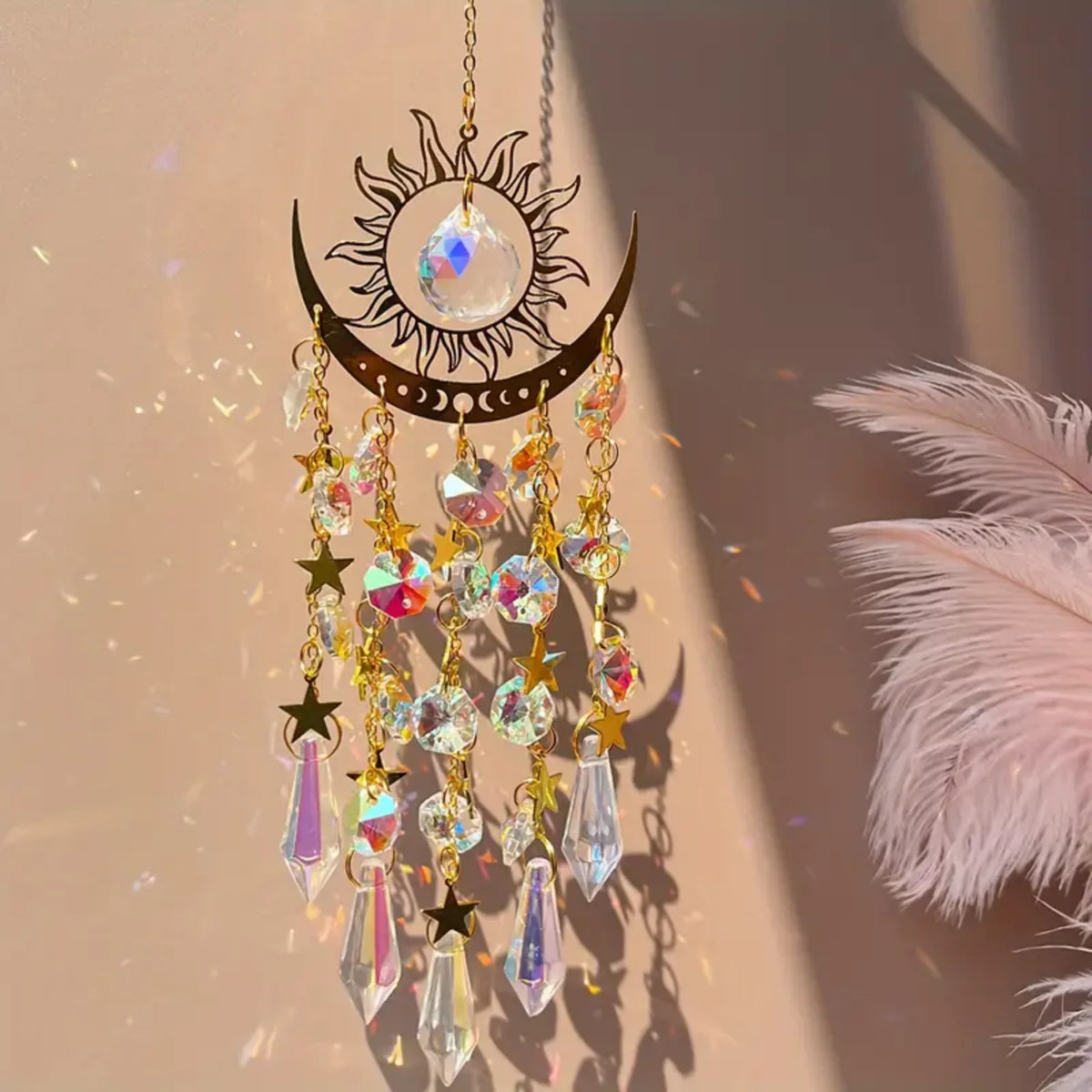 A hanging gold star moon wind chime decoration with clear crystal drops and a feather in soft sunlight.