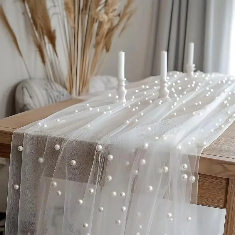 White pearl gauze fabric draped over a wooden table with beaded trim and white candles.