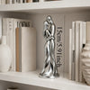 A silver sculpture of a couple embracing, displayed on a white shelf among books.
