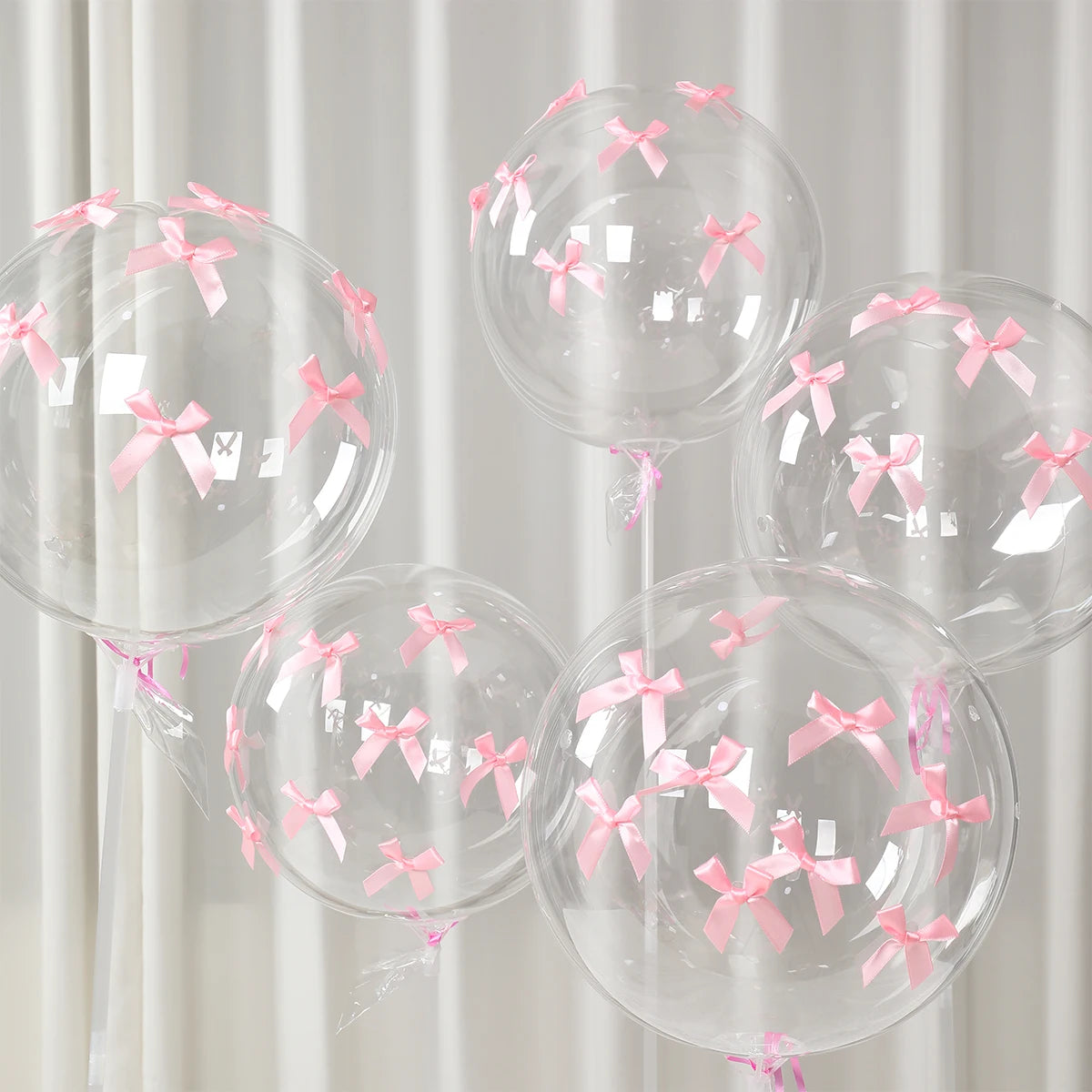 A set of clear latex balloons tied with pink ribbon bows, suitable for celebrations.