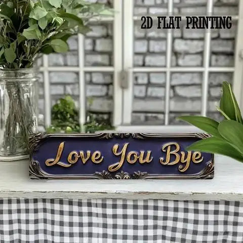 A dark blue vintage metal sign with the text Love You Bye is displayed on a white surface.