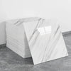 A stack of white marble tile stickers showing gray veining on a gray concrete floor.