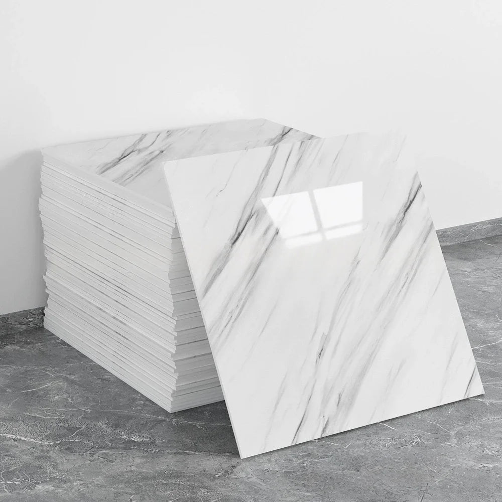A stack of white marble tile stickers showing gray veining on a gray concrete floor.