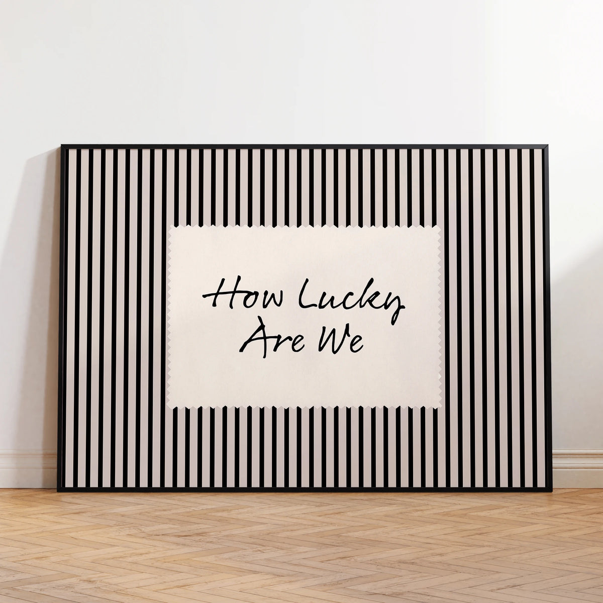 Black framed canvas wall art featuring the text How Lucky Are We on a white background with vertical black stripes.