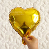 A golden heart-shaped foil balloon is being held, set against a white quilted background.