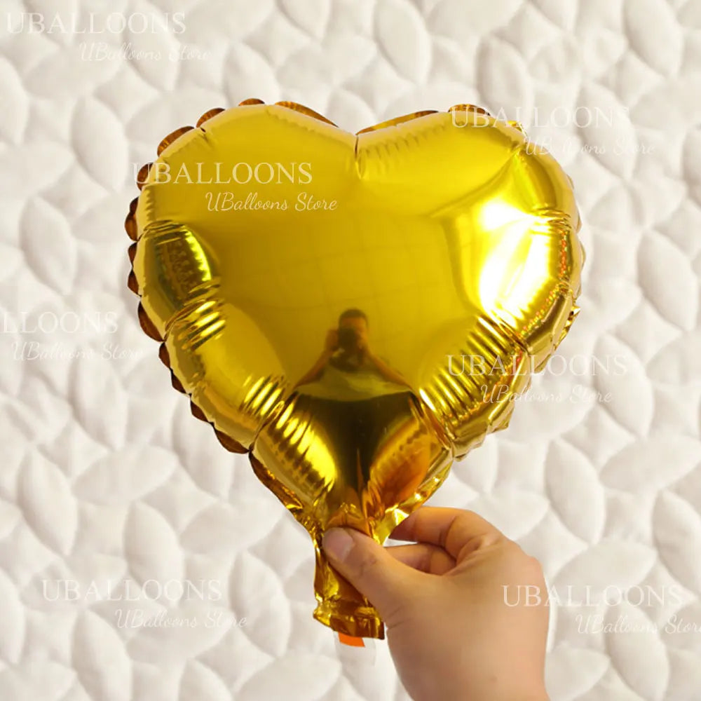 A golden heart-shaped foil balloon is being held, set against a white quilted background.