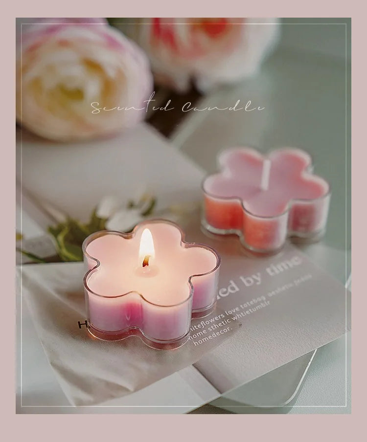 A pink flower-shaped tea light candle in a glass holder resting on white paper.