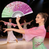 A woman performs a dance while holding a large pink and green plastic folding fan.