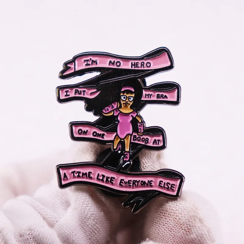 A black enamel pin badge featuring a stylized illustration of a person and text that reads I'm no hero I put my bra on one bo