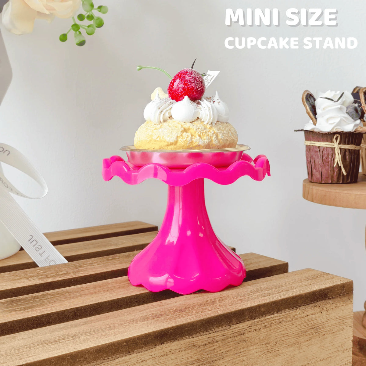 A pink mini cupcake stand displaying a single cupcake topped with whipped cream and a red berry.