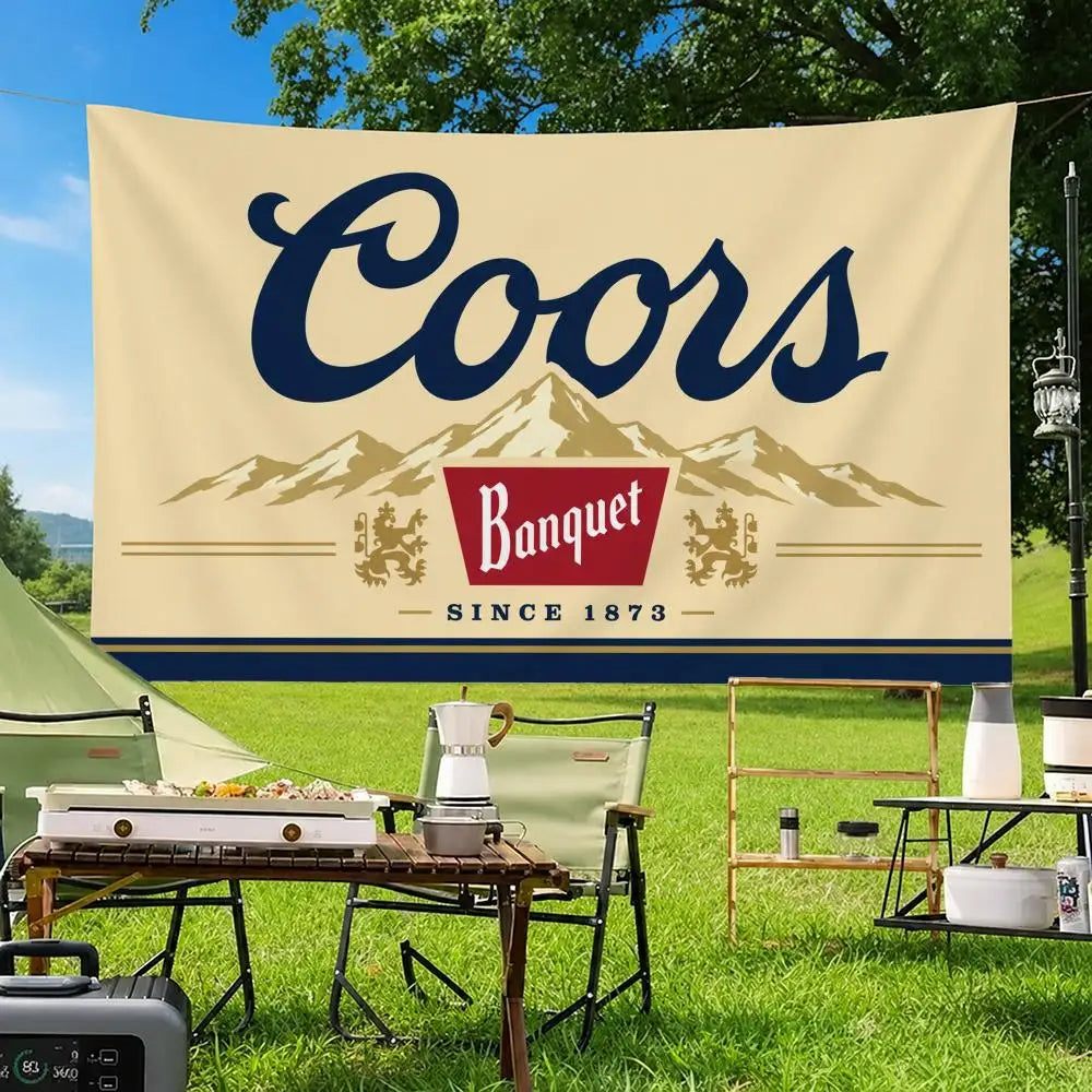 A beige flag banner with the word Coors in dark blue script is displayed outdoors on a grassy field.