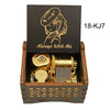 A wooden box containing a brass music box with a gold-colored mechanism and an anime character design.