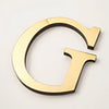 A gold acrylic mirror letter G wall sticker with a black outline and a pointed bottom section.