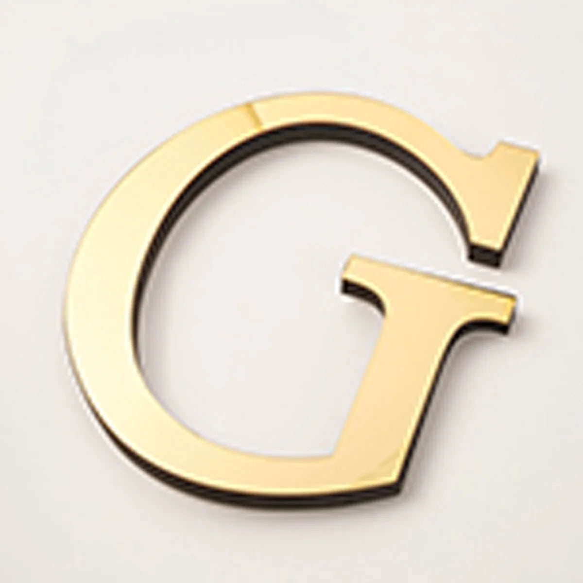 A gold acrylic mirror letter G wall sticker with a black outline and a pointed bottom section.
