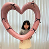 A young girl is holding a large pink heart-shaped balloon decoration with black ribbons.