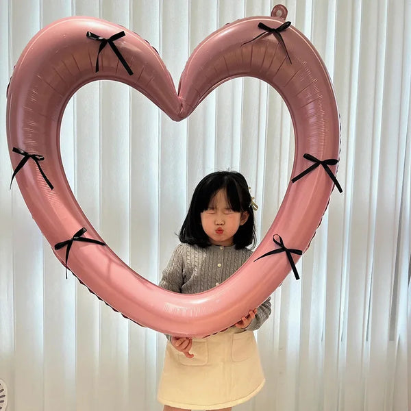 A young girl is holding a large pink heart-shaped balloon decoration with black ribbons.