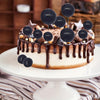 A round cake decorated with chocolate drizzle and black foam ball toppers for party display.