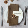 A set of handcrafted fringed cotton napkins is displayed on a white plate with a wooden fork and a slice of citrus fruit.