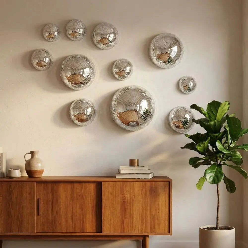 A collection of silver disco ball-shaped wall decor mounted on a white wall above a wooden cabinet and a potted plant.