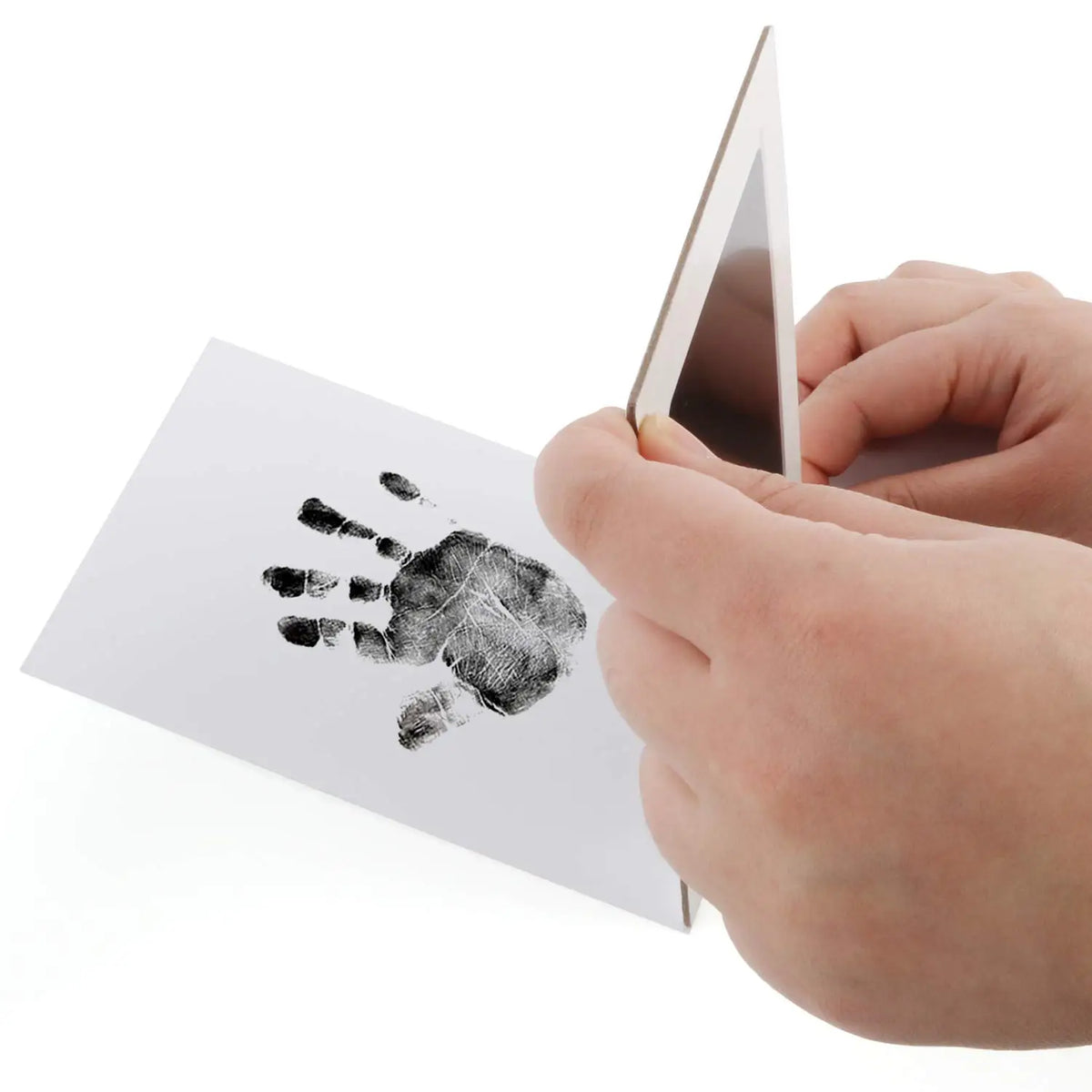 A hand holds a white card featuring a black ink pet paw print, next to a triangular wooden piece.