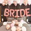 A pink and gold foil balloon arch spelling the word BRIDE decorated with white and pink balloons.