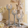 A silver metal glass candle holder stands next to a white flower arrangement and a statue of an angel.