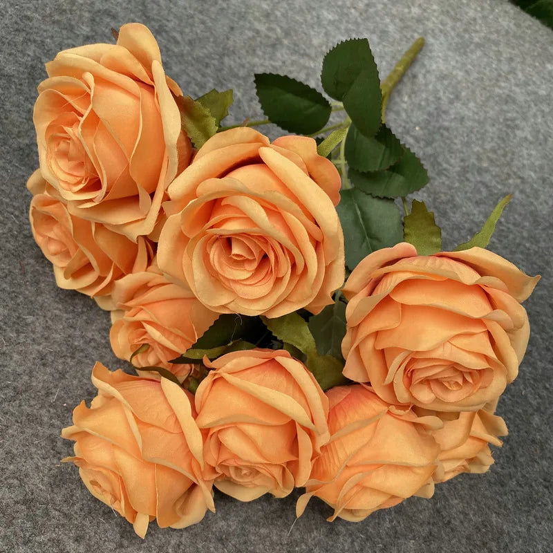 A bouquet of nine realistic silk orange roses arranged on a gray background.