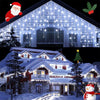 String lights draped across a house facade and a decorated Christmas tree in a snowy outdoor scene