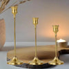 A set of three ornate vintage gold metal candle holders displayed on a wooden slab.