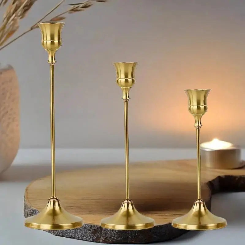 A set of three ornate vintage gold metal candle holders displayed on a wooden slab.