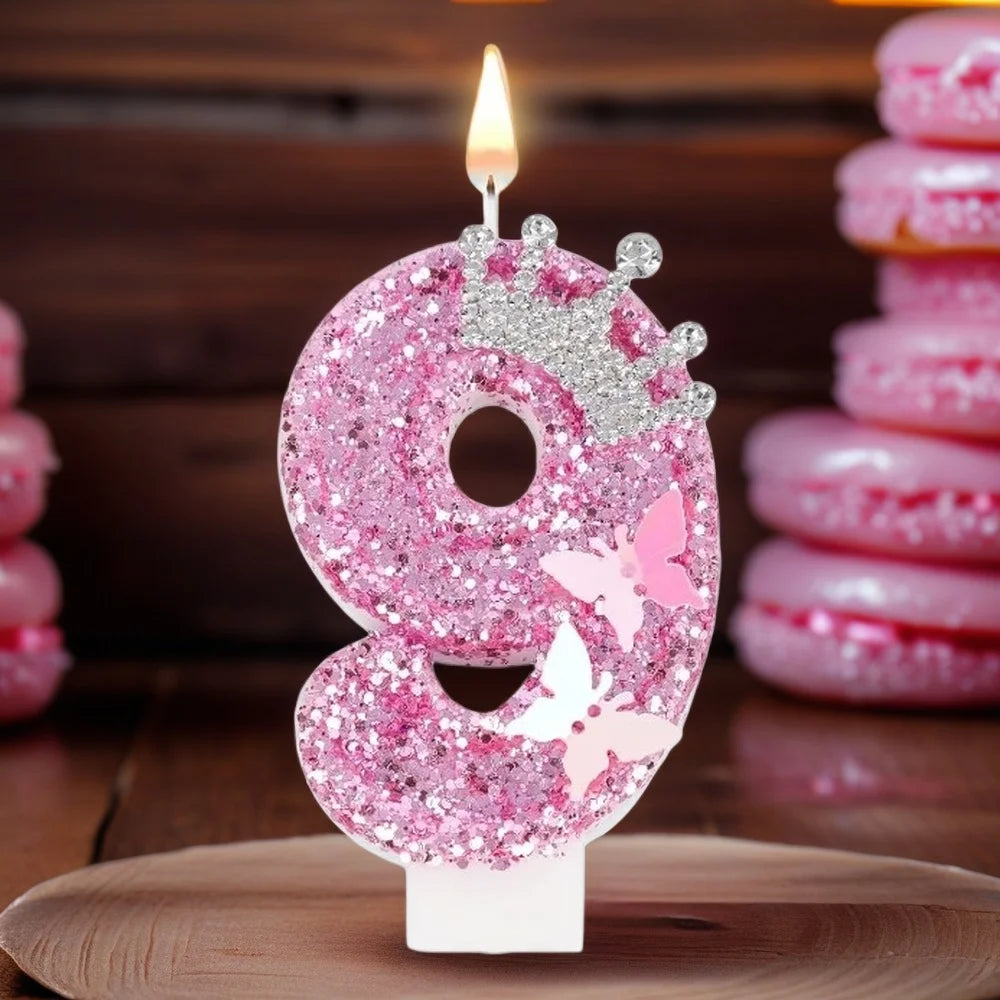A pink glitter candle shaped like the number 9 with a crown, lit on a wooden surface.