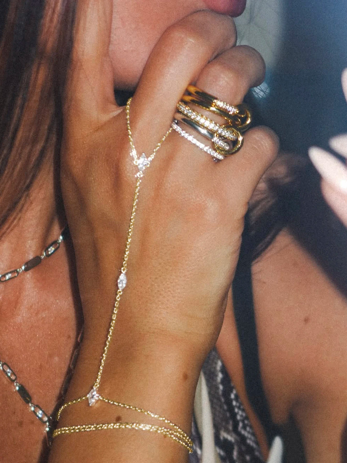 A close-up of a hand wearing multiple gold and diamond layering chain bracelets on the wrist.