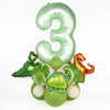 A set of foil balloons shaped like the number three and various dinosaur figures in avocado green and orange for birthday dec