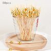 A glass bowl filled with 50 bamboo fruit skewers topped with gold-colored spherical beads.