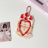 A pink and white cartoon strawberry heart shaped bag keychain card holder with a red strawberry charm.
