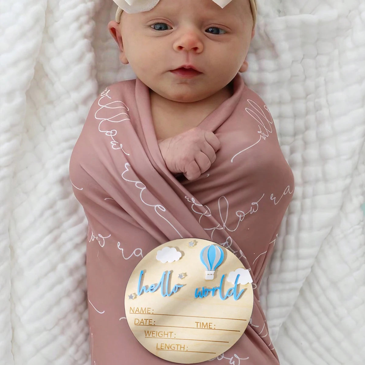 A newborn birth announcement sign featuring a baby wrapped in pink fabric with white text and a cloud-shaped disk.