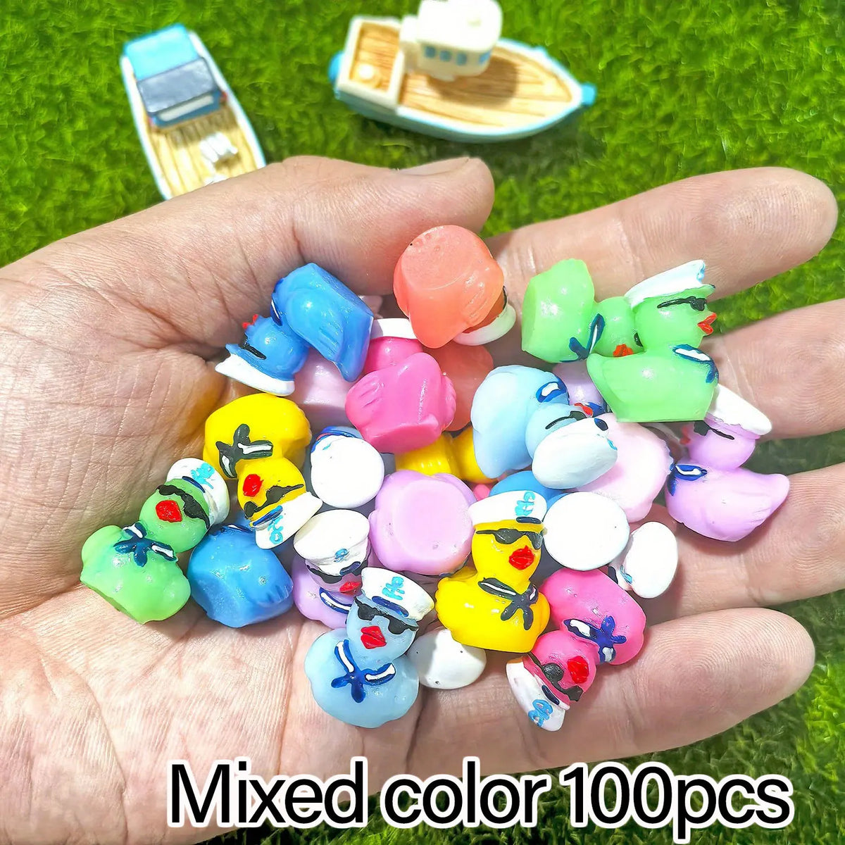 A hand holds a mixed color set of 100 mini resin cruise ducks with sunglasses