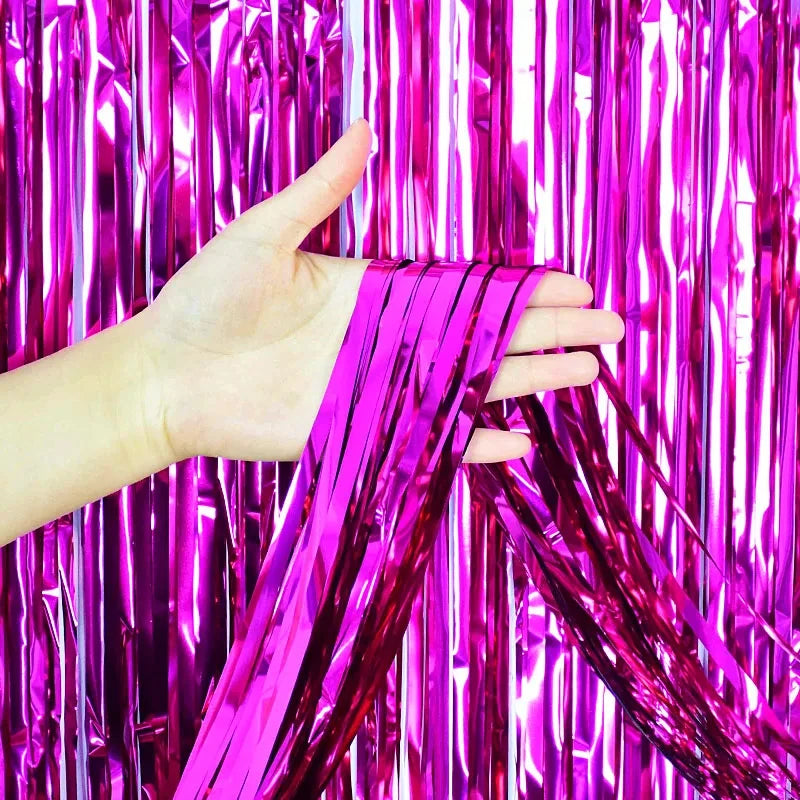 A hand is holding a piece of metallic pink foil fringe fabric against a vibrant magenta curtain background.