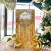 A golden metallic foil fringe curtain backdrop decorated with a Merry Christmas sign and gold ornaments.