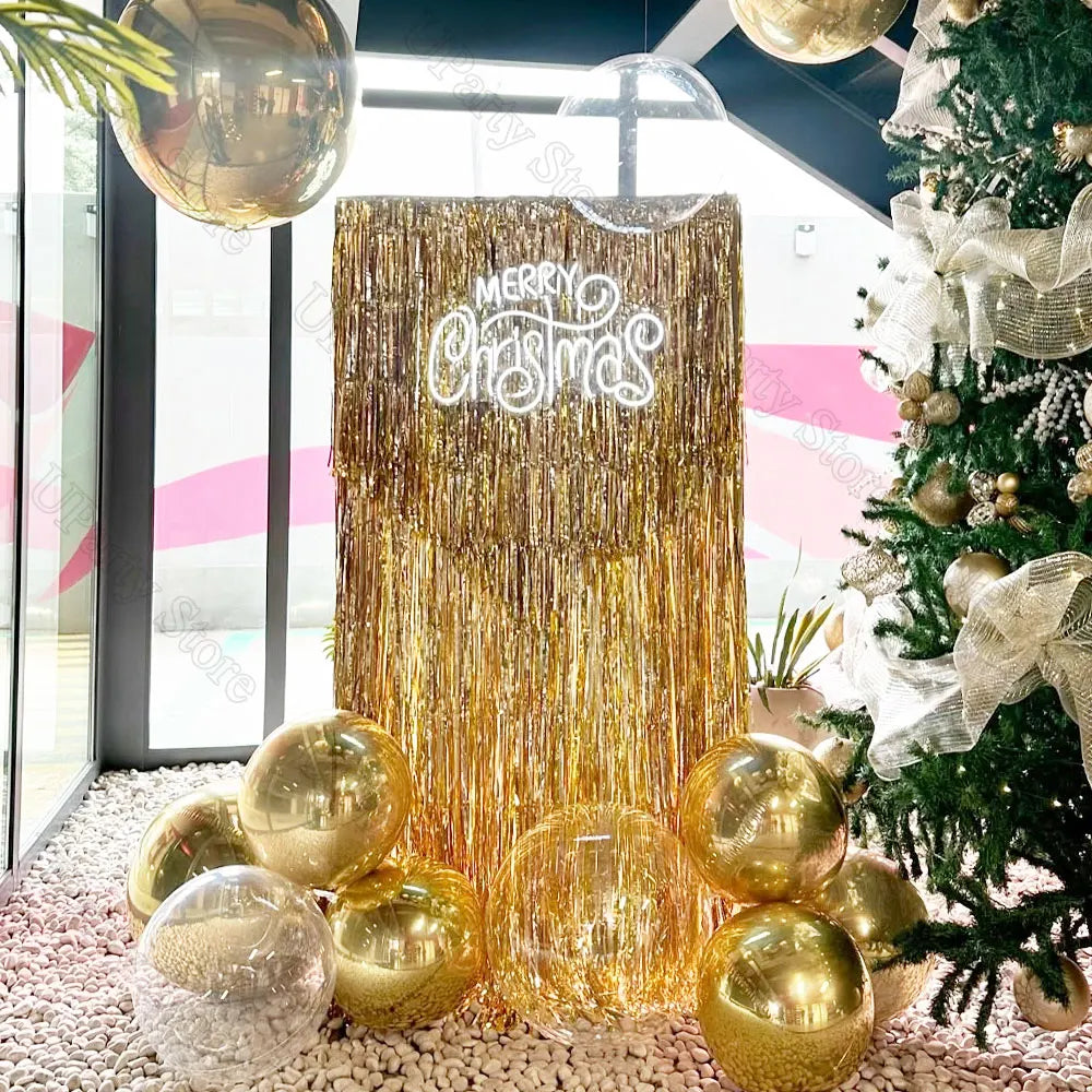 A golden metallic foil fringe curtain backdrop with a Merry Christmas sign and gold ornaments for party decor.