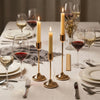A set of modern metal taper candles displayed on a table setting with wine glasses and plates.