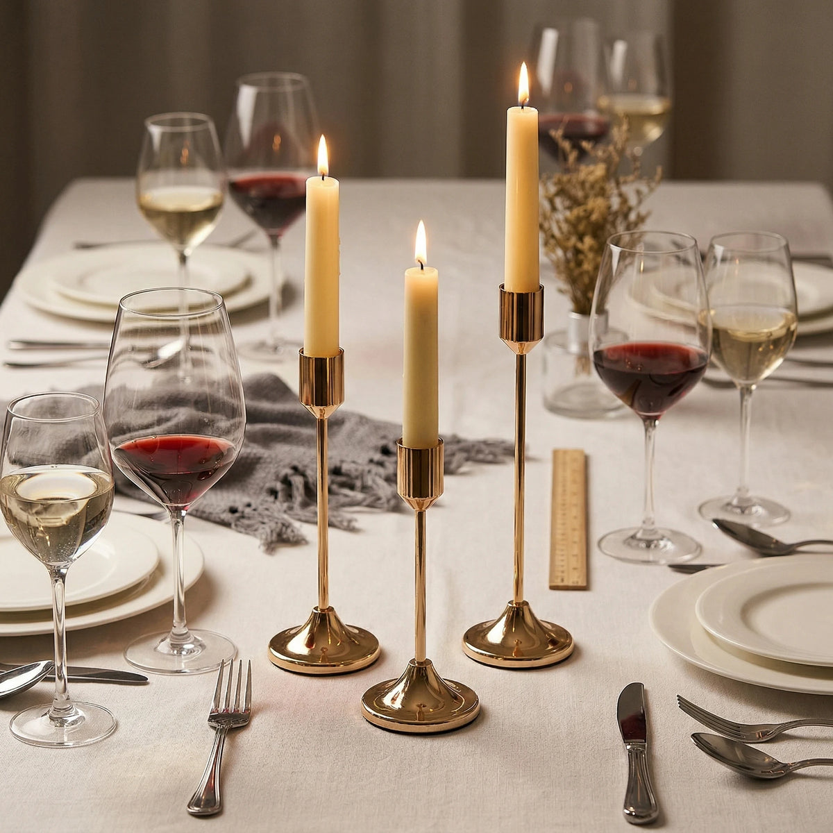A set of modern metal taper candles displayed on a table setting with wine glasses and plates.