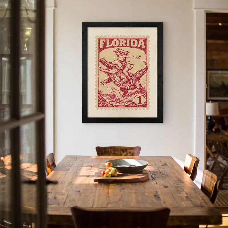 A framed vintage western art print featuring a silhouette of a cowgirl riding a dinosaur against a red background.