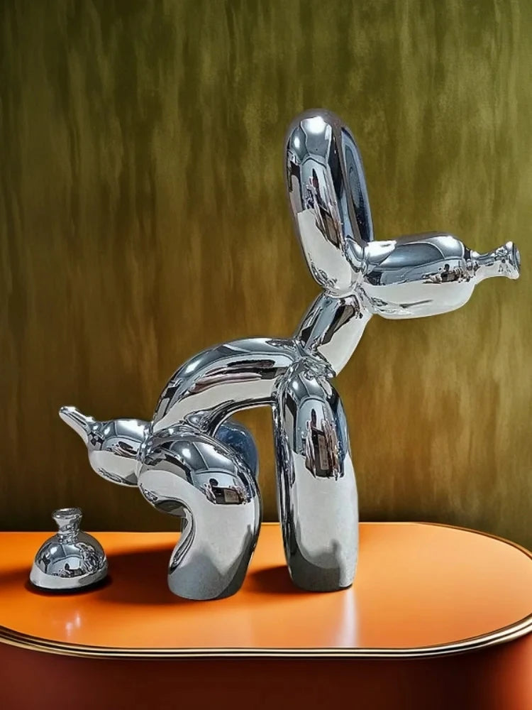 A chrome sculpture of a dog squatting, displayed on an orange surface against a muted green background.