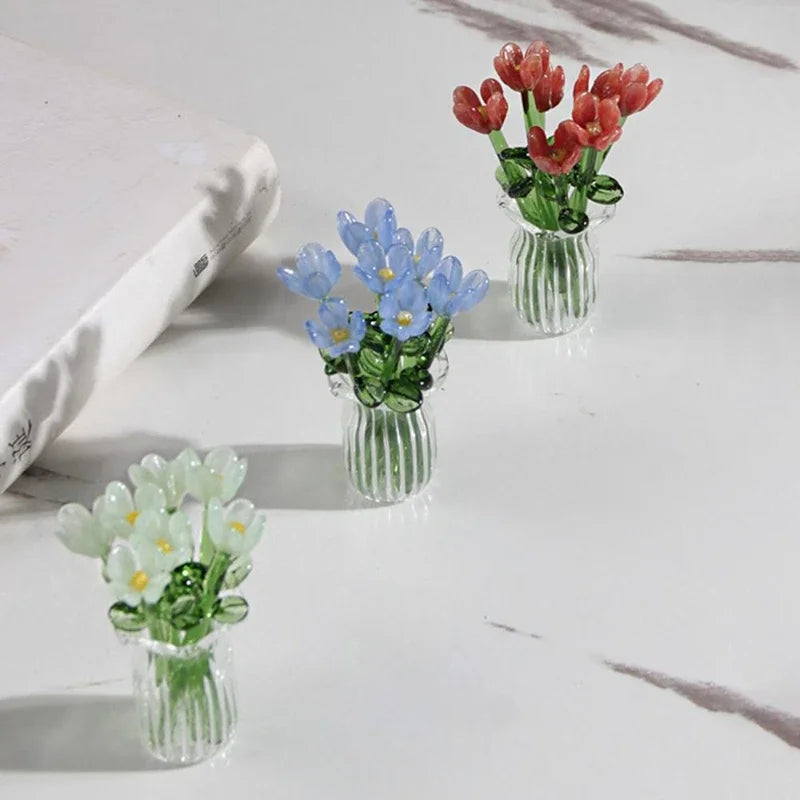 Three miniature glass flower sculptures in shades of red, blue, and green are displayed on a white surface.