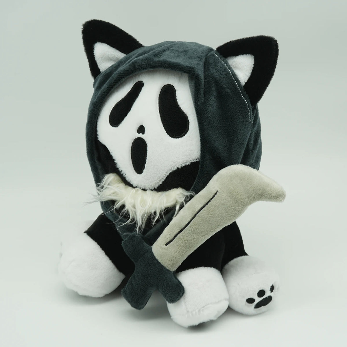 A plush toy resembling a cat with black and white markings wearing a dark hood and holding a blade.