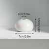 A white ceramic mini vase with a smooth, rounded shape is shown on a light surface.
